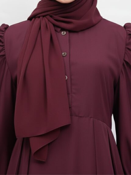 Close-up of a burgundy abaya with puffed sleeves and a matching scarf, featuring button detailing on the front.